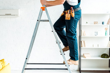 cropped view of installer in overalls climbing ladder - obrazy, fototapety, plakaty