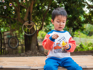 Asian child boy playing bubbles outdoor with happy concentrate face  with natural rural green background. Young kid have fun in relaxing holiday.