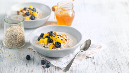 Oatmeal porridge with almond milk, mango, blueberries, seeds, almonds and honey in a plate, light background, copy space. Vegan food, healthy fitness breakfast. Plant based concept. Proper nutrition.