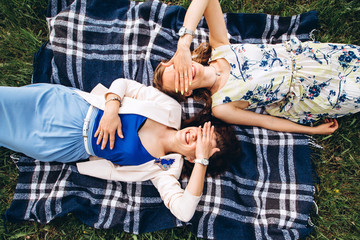 Two pretty girls lie on a blue plaid outdoors in the park, summer picnic. Girlfriends' girls have...