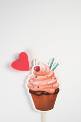 Muffin with cream, cherry and pink heart of paper color on a white background, the concept for Valentine's Day, wedding, birthday and other holidays, view from the top.