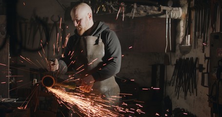 Young blacksmith with angle grinder in his workshop