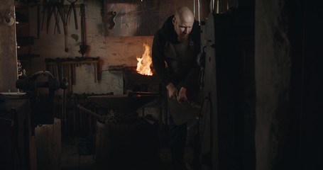 Blacksmith hammering heated iron with forging hammer machine and making a knife in his workshop at night