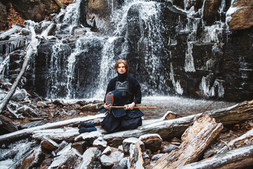 Fototapeta na wymiar Man practicing kendo with bamboo sword on waterfall background. Place for text or advertising