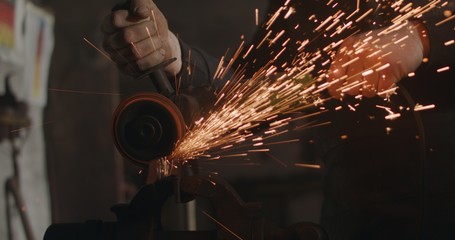 Blacksmith with angle grinder in his workshop sparks flying dark closeup
