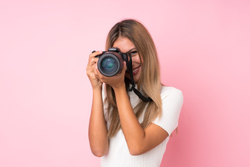 Young blonde woman over isolated pink background with a professional camera - obrazy, fototapety, plakaty