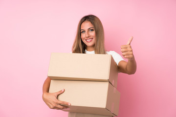Young blonde woman over isolated pink background holding a box to move it to another site with...