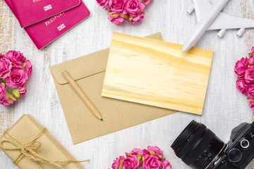 Mockup blank wooden card and envelop on grunge white wood for travel with valentines day & love season background concept. Top view of mock up with rose flowers, craft roses, passport, camera