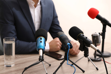 Businessman giving interview at table with microphones, closeup. Journalist conference