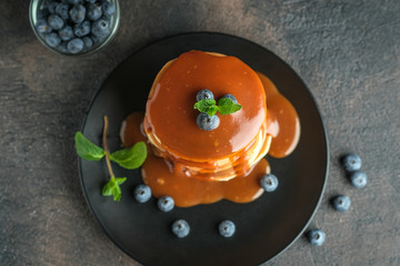 Delicious pancakes, with fresh blueberries, strawberries and caramel on a dark background. Top view.