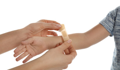 Mother putting sticking plaster onto son's arm on white background, closeup