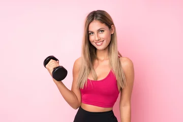 Fotobehang Young sport blonde woman over isolated pink background making weightlifting with kettlebell © luismolinero