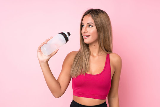 Young sport blonde woman over isolated pink background with sports water bottle © luismolinero
