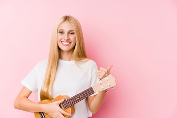 Fototapeta premium Young blonde girl playing ukelele smiling and raising thumb up