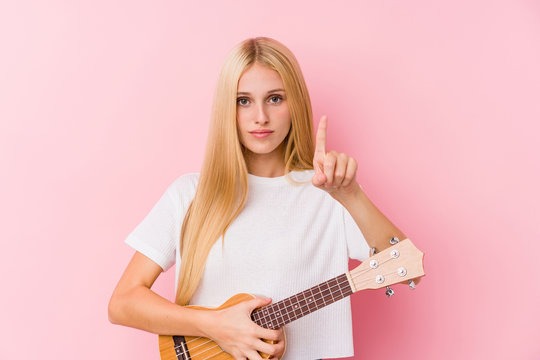 Young blonde girl playing ukelele showing number one with finger.