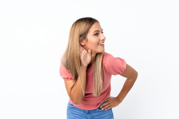 Young blonde woman over isolated white background listening to something by putting hand on the ear