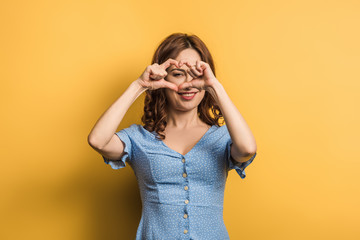 cheerful girl showing heart with hands on yellow background