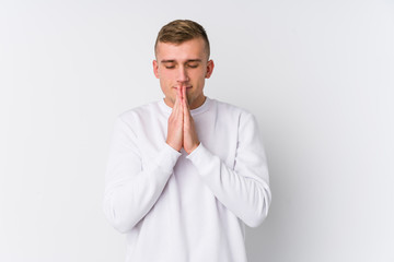 Young caucasian man on white background holding hands in pray near mouth, feels confident.