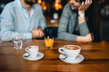 close up of cappuccino and espresso coffee in restaurant, happy couple in blurred background
