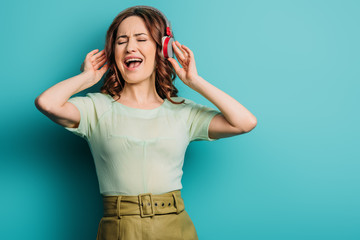 cheerful girl singing in wireless headphones with closed eyes on blue background