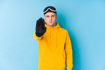 Young skier man standing with outstretched hand showing stop sign, preventing you.