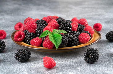 Fresh ripe organic raspberries and blackberries in a bowl on a gray background