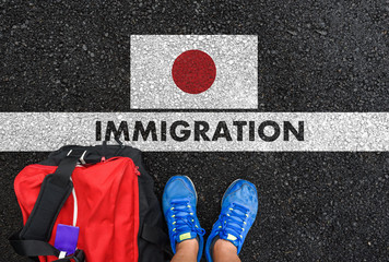 Man in shoes with bag standing next to line with word IMMIGRATION and flag of Japan on asphalt road