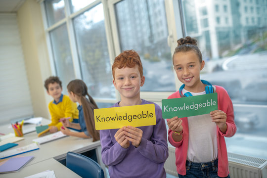 Two smiling kids holding the word knowledgeable