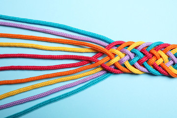 Braided colorful ropes on light blue background, top view. Unity concept