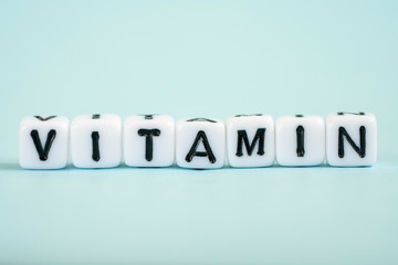 Vitamin word from white cubes on blue background. Vitamins A B C D E, healthy and medical concept.