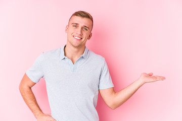 Young caucasian man isolated showing a copy space on a palm and holding another hand on waist.