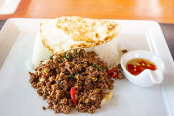 Pad Krapao Beef,  (Stir fried minced beef with thai basil and chilli) top up with sun rise side up eggs on the white dish. close up 