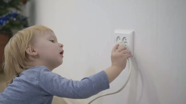 child tries to insert a power plug into the electric socket close-up, a small boy dangerously playing at home