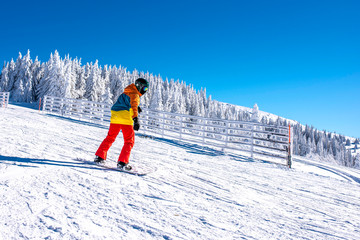 Fototapeta na wymiar Snowboarder riding snowboard in mountain ski resort with beautiful winter landscape in the background