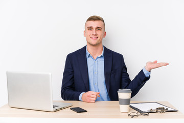 Young business man with a laptop showing a copy space on a palm and holding another hand on waist.