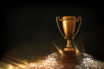 low key image of trophy over wooden table and dark background, with abstract shiny lights