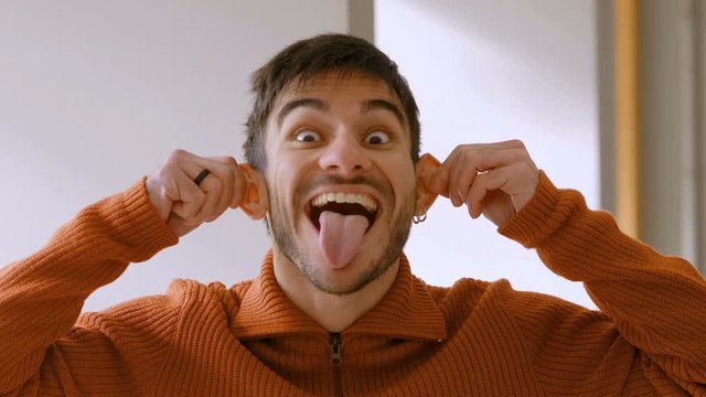 young man makes fun sticking his tongue out and pulling his ears
