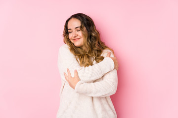 Young curvy woman posing in a pink background isolated hugs, smiling carefree and happy.