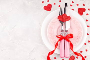 Festive Table with White and Pink Plates with Fork, Knife and Red Ribbon Bow with Decorative Handmade Hearts for Love Dinner on Concrete Background. Valentine's Day Concept. Copy Space and Top View