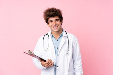 Young caucasian man over isolated pink background with doctor gown and holding a folder