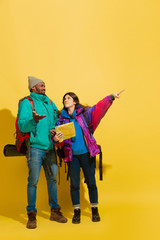Get agreement in way choosing. Portrait of a cheerful young tourist couple with bags isolated on yellow studio background. Preparing for traveling. Resort, human emotions, vacation, friendship, love.