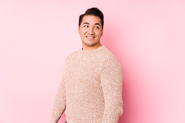 Young curvy man posing in a pink background isolated looks aside smiling, cheerful and pleasant.