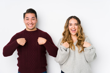 Young couple posing in a white background surprised pointing with finger, smiling broadly.