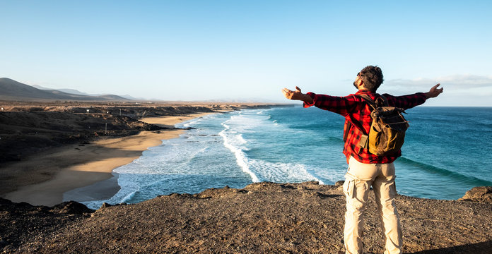 Standing man enjoying the travel and nature landscape in front of him - coastline with awesome beach and  noboy there - alternative traveler backapck lifestyle vacation - outdoor leisure people
