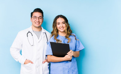 Young doctor couple posing in a blue background isolated happy, smiling and cheerful.