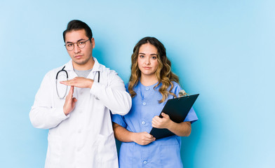 Young doctor couple posing in a blue background isolated showing a timeout gesture.