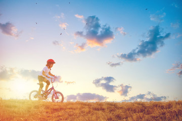 Little girl with biking at sunset on the hills
