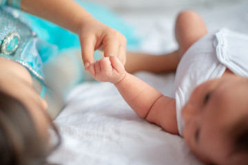 newborn baby with her older sister together on the bed holding each other`s hand