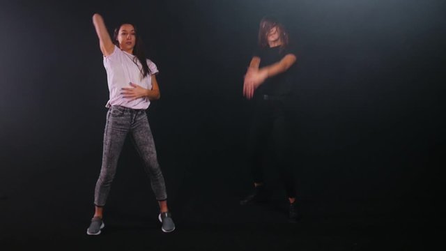Two young women freestyle dancing in dark studio
