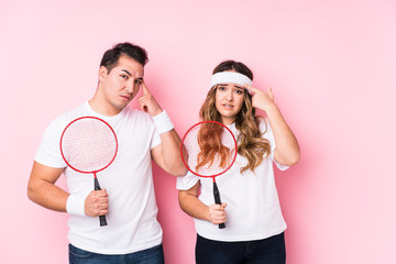 Young couple playing badminton isolated showing a disappointment gesture with forefinger.